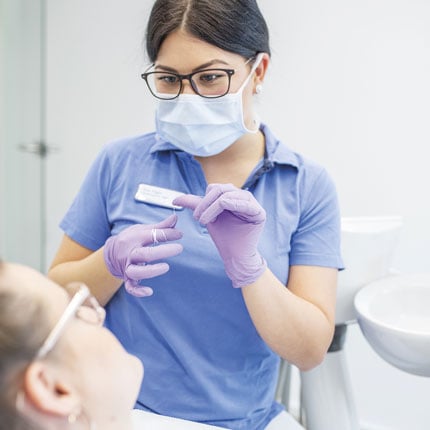 Dentalhygienikerin zeigt Patientin die richtige Verwendung von Zahnseide