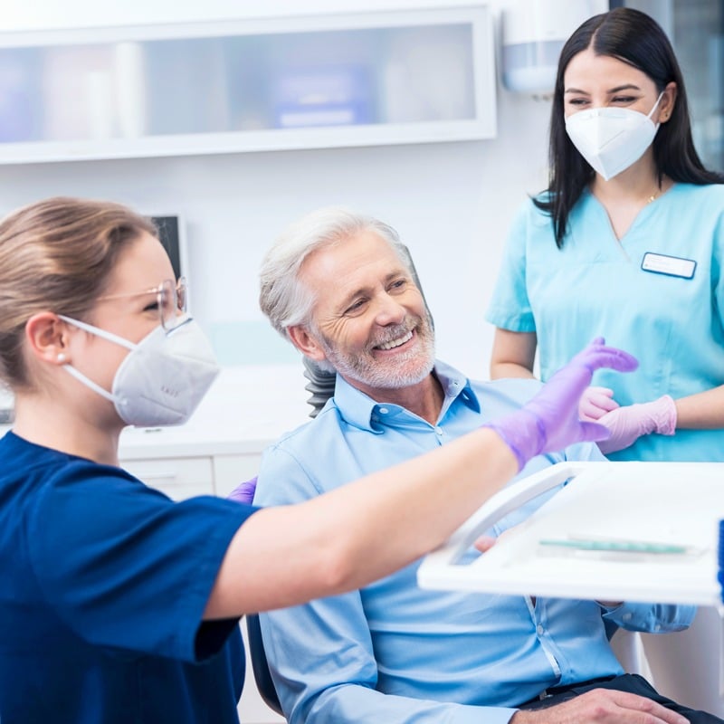 Zahnärztin, Patient und zahnmedizinische Fachangestellte im Behandlungszimmer